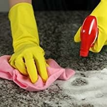 Person cleaning a countertop with gloves and spray.